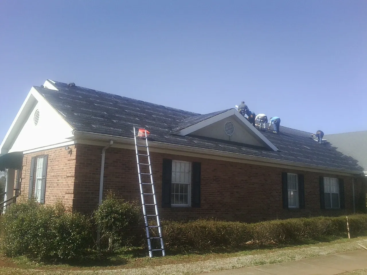 Crew tearing shingles off a brick ranch roof with a ladder set — Emergency Roof Repair work by our crew in Trout Run