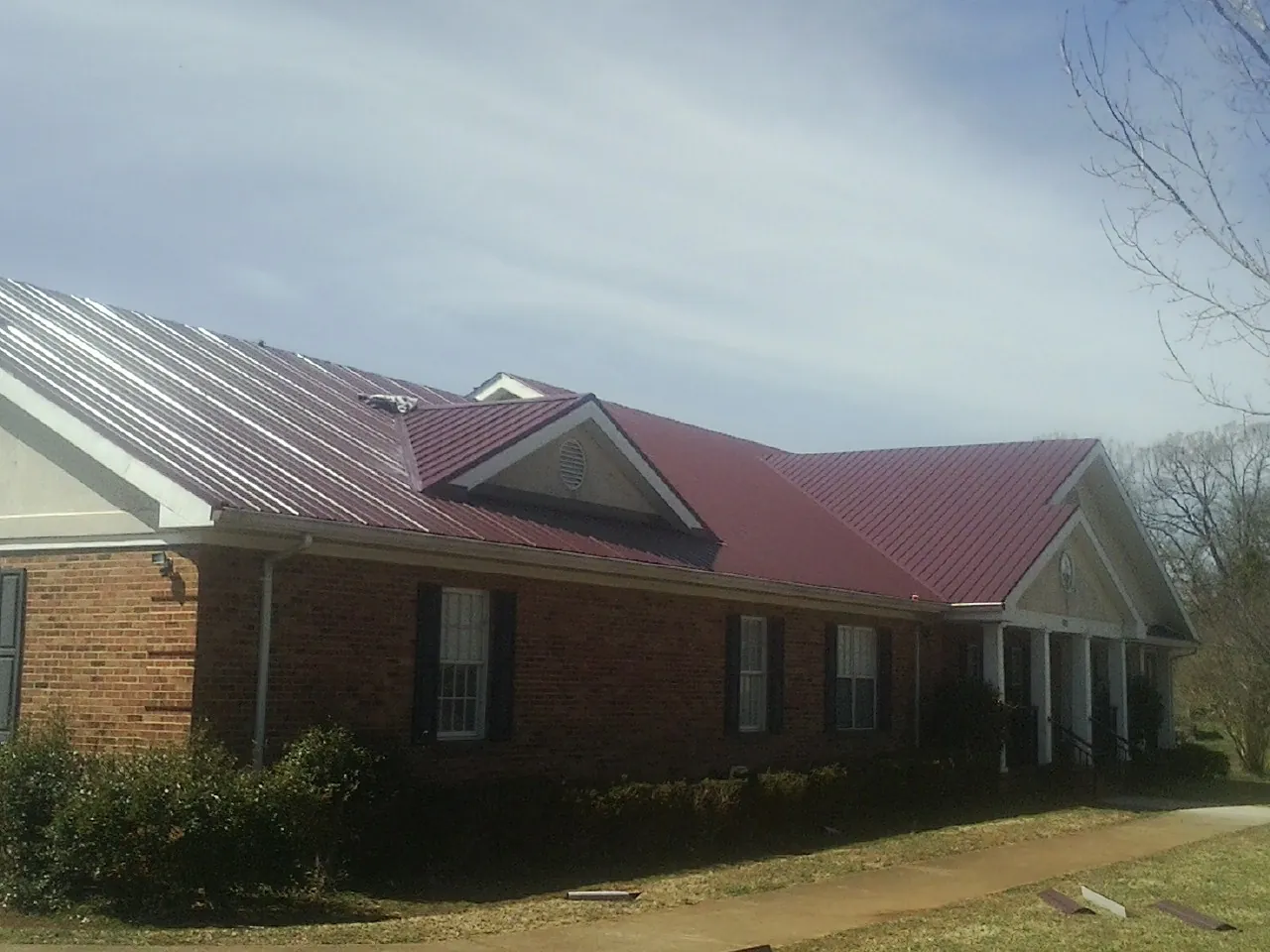 Red metal roof with gabled entries on a long brick building, from a Hail Damage Roof Repair job in Trout Run