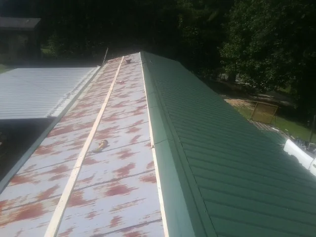 Old rusted panels beside newly installed green metal roofing — Wind Damage Roof Repair by Roofing Brothers in Trout Run