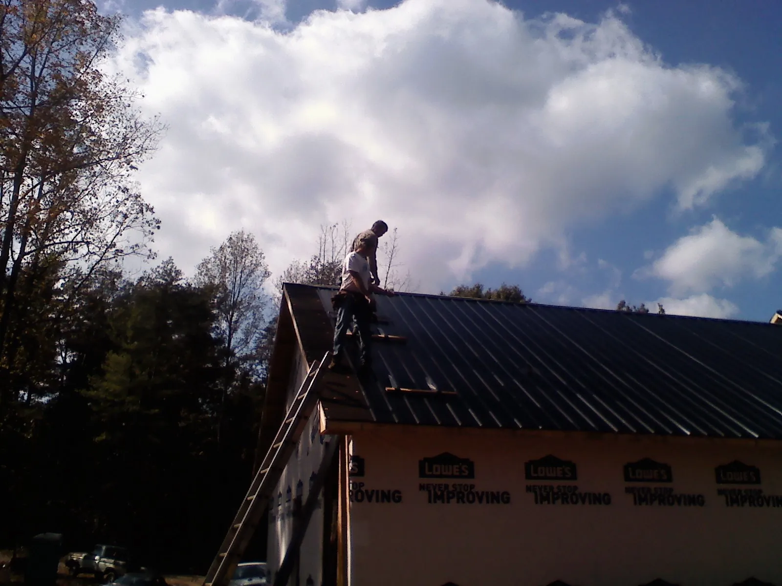 Roofer fastening dark metal panels high against a cloudy sky, from a Roof Inspection job in Trout Run