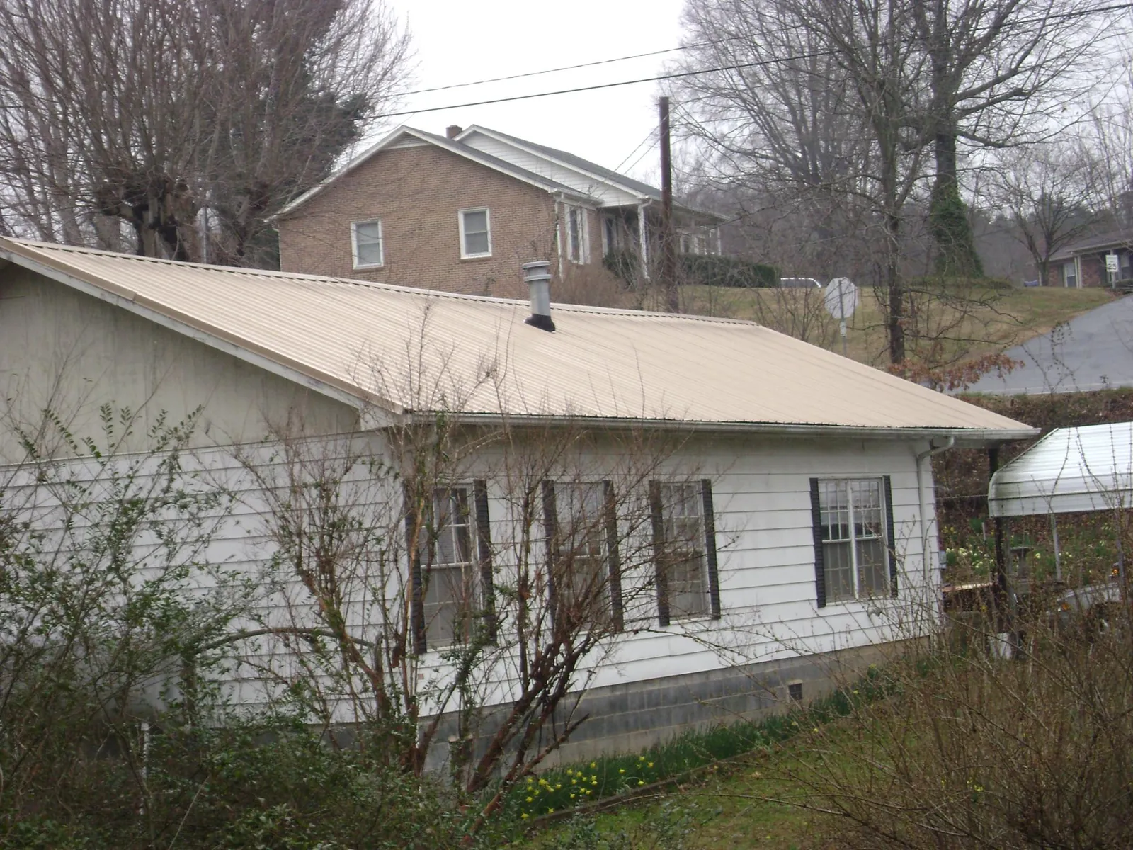 Tan metal roof on a white sided house set into a hillside — Commercial Roofing by Roofing Brothers in Trout Run